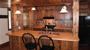 A wooden kitchen with a central island, two black chairs, and pendant lights. - Beautiful Lakefront Condo with boat slip, pool access and great location! (Osage Beach)