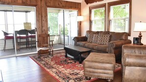 A cozy living room with a brown leather sofa, a matching ottoman, and a wooden coffee table. A patterned rug covers the floor, and there are two chairs with red cushions. - Beautiful Lakefront Condo with boat slip, pool access and great location! (Osage Beach)