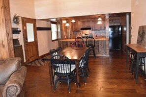 A spacious dining area with a wooden table and chairs, a kitchen with wooden cabinets and a refrigerator, and a cozy living area with a leather sofa.