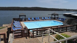 A swimming pool with blue lounge chairs, a wooden deck, and a view of a lake. - Beautiful Lakefront Condo with boat slip, pool access and great location! (Osage Beach)