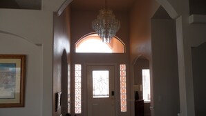 Ein Korridor mit einer Chandelier, einer Tür mit Buntglasfenstern und einem gerahmten Bild an der Wand.