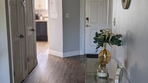 A hallway with wooden flooring, a glass table with a vase, and a decorative sculpture. - St. Pete Beach / Isla Del Sol -  2 bedroom 2 bath Condo (St. Petersburg)