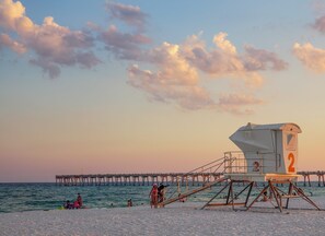 A lifeguard tower with a number 2 sign, a pier extending into the sea, and people on the beach.
