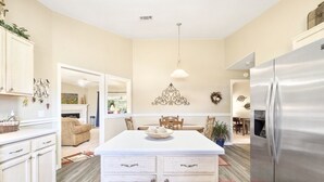 A kitchen with a central island, white cabinets, a stainless steel refrigerator, and a dining area with a table and chairs. - Private Pensacola Getaway Minutes to Perdido Key! (Pensacola)