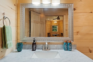 A bathroom with a wooden interior, a large mirror with a decorative frame, a sink, and two bottles of shampoo.