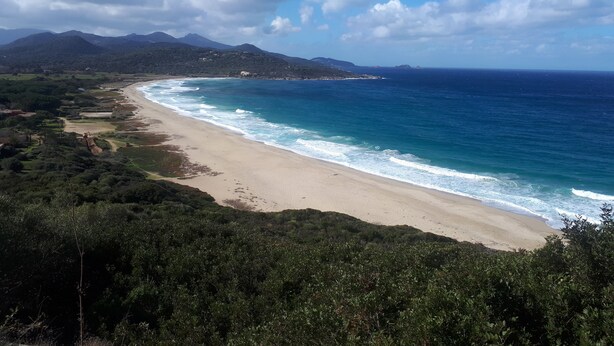 Un paisaje costero con playa, océano y montañas al fondo.