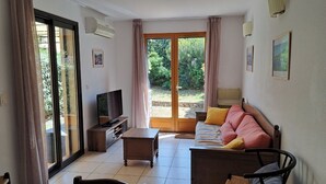 Una sala de estar con sofá, televisor, mesa de centro y puerta corrediza de vidrio que da a un jardín.