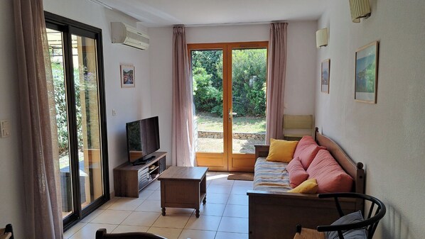 A living room with a sofa, a TV, a coffee table, and a sliding glass door leading to a garden.