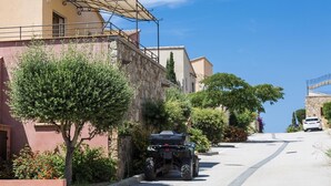 Una calle estrecha con una moto de cuatro ruedas estacionada, edificios de piedra y un cielo azul despejado.