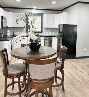 A modern kitchen with white cabinets, a black refrigerator, and a round dining table with chairs.
