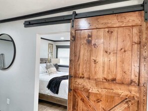 A bedroom with a bed, a wooden door, and a mirror on the wall.