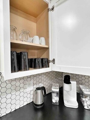 A kitchen with a white cabinet, a coffee maker, a kettle, and a honeycomb-patterned backsplash.
