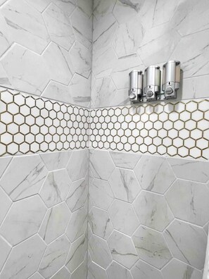 A bathroom with hexagonal marble tiles, a gold-tinted hexagonal tile border, and a wall-mounted faucet.