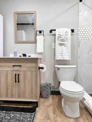 A modern bathroom with a wooden vanity, white toilet, and a hexagonal tile backsplash.