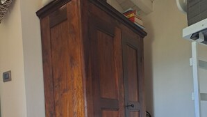 Une chambre avec une armoire en bois, un lit recouvert d’une couette blanche et un radiateur blanc.