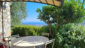 Une terrasse extérieure avec une table ronde et des chaises, un mur en pierre et une vue sur la mer.