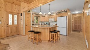 A kitchen with wooden cabinets, a central island with stools, a refrigerator, and pendant lighting. - Lakefront Whitefish Chain Retreat - Sleeps 15 - Pontoon - Fall Getaway & Rates (Crosslake)