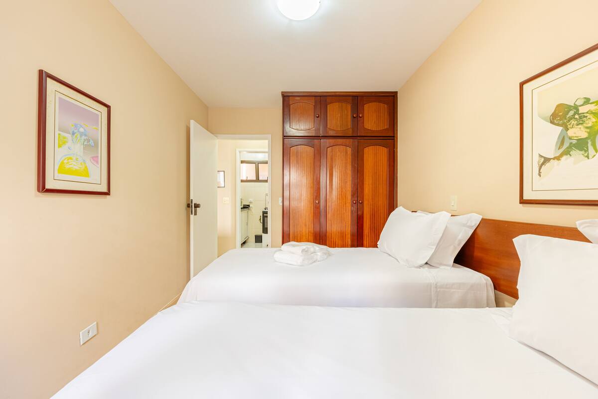 A hotel room with two beds, wooden wardrobe, and framed artwork on the walls.