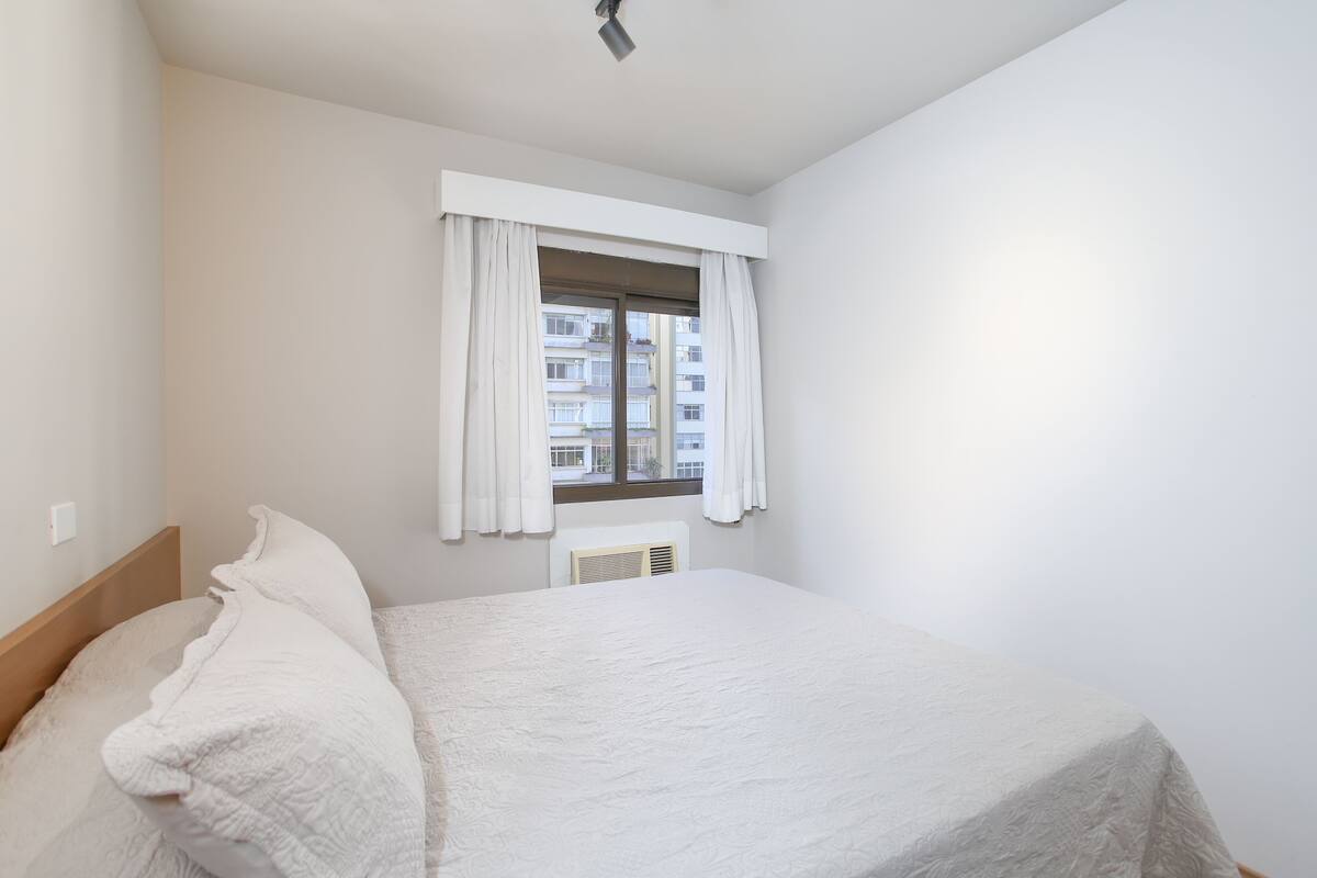 A bedroom with a bed, a window with curtains, and a radiator.