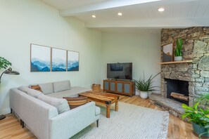 A living room with a sofa, coffee table, TV, fireplace, and artwork on the wall. - AVL Canopy House - 12 minutes to DT Asheville. Child, Infant, Dog Friendly  (Weaverville)
