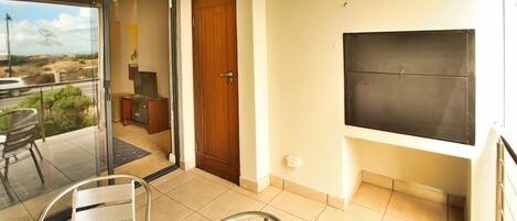 A balcony with a glass door leading to a patio area, a wooden door, a flat-screen TV mounted on the wall, and a chair.