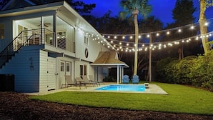 A two-story house with a covered patio, a swimming pool, and string lights. - Luxury Beach House - Group/Family/Dog Friendly (Hilton Head Island)