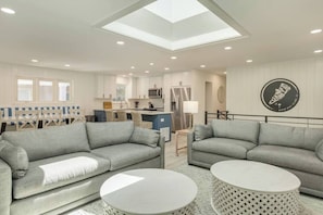 A modern living room with two grey sofas, a small white coffee table, and a dining area with a blue table and white chairs.
