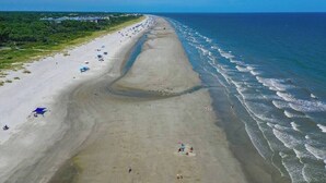 An aerial view of a beach with a long stretch of sand, a few umbrellas, and people scattered along the shoreline. - Luxury Beach House - Group/Family/Dog Friendly (Hilton Head Island)