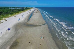 An aerial view of a beach with a long stretch of sand, a few umbrellas, and people scattered along the shoreline.
