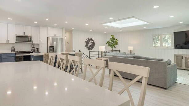 A modern kitchen with white cabinets, a dining table, and chairs. There is a gray sofa and a small plant in the living area. - Luxury Beach House - Group/Family/Dog Friendly (Hilton Head Island)
