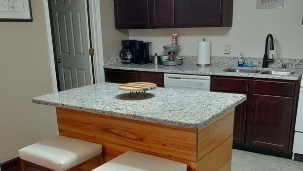Una cocina con una isla central, dos taburetes de bar, armarios de madera oscura, una cafetera y un fregadero.