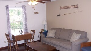 Una sala de estar con una mesa de comedor, sillas, un sofá, una lámpara y un adorno de pared.