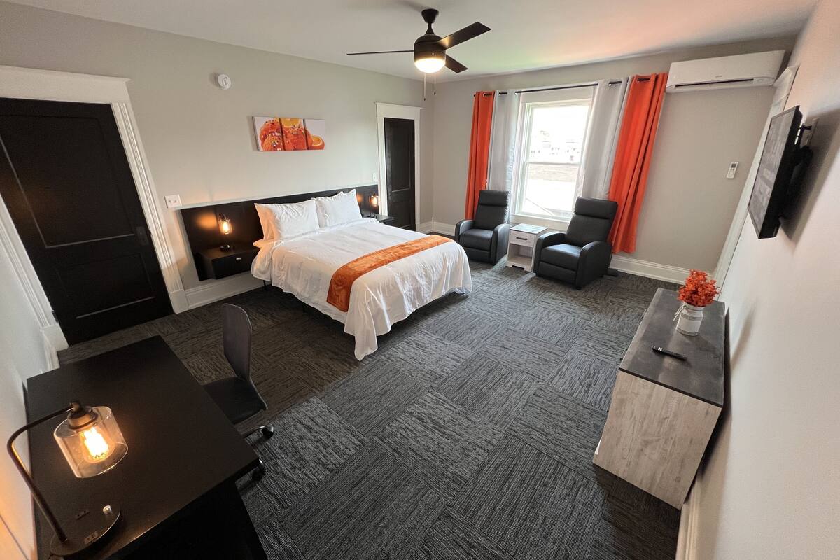 Een hotelkamer met een bed, twee fauteuils, een bureau, een televisie en een plafondventilator.