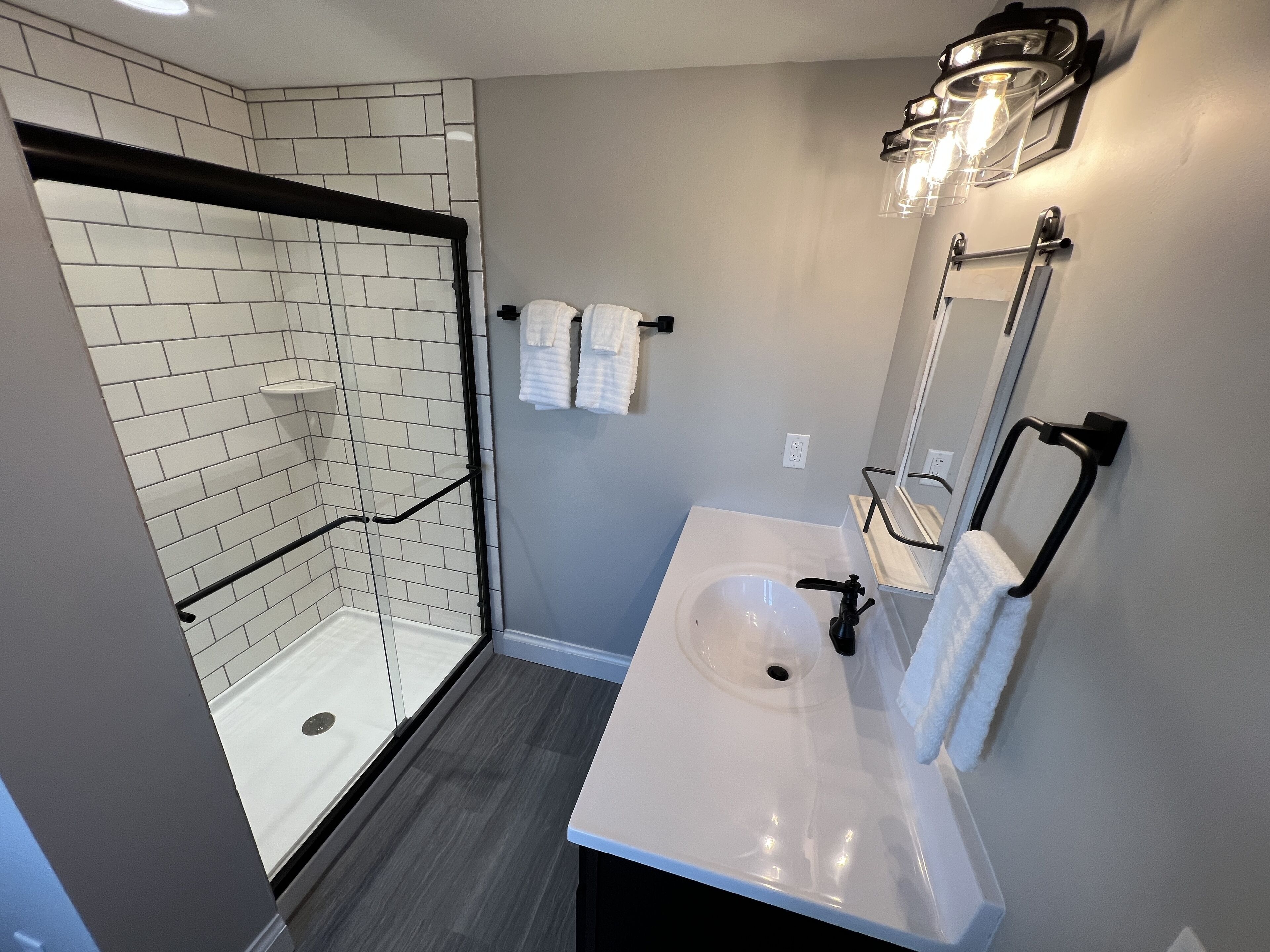 A modern bathroom with a walk-in shower, a white sink, and a mirror with lights.