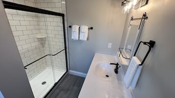 Un baño moderno con cabina de ducha, un lavabo blanco y un espejo con luces.