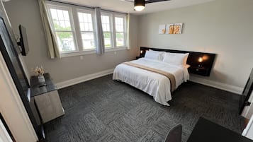 Un dormitorio con cama, escritorio, silla, ventilador de techo y ventana con cortinas.