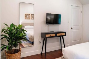 A bedroom with a bed, a television mounted on the wall, a bedside table, a mirror, and a potted plant. - Modern Farmhouse Getaway I 2 BR, Sleeps 6 (Elizabethtown)