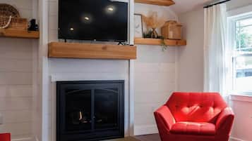 A living room with a flat-screen TV mounted above a fireplace, a red armchair, and wooden shelves with decorative items.