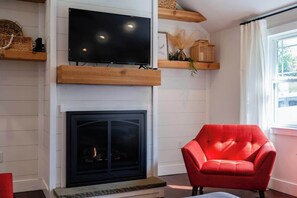 Ein Wohnzimmer mit Flachbildfernseher über einem Kamin, einem roten Sessel und Holzregalen mit Dekorationen.