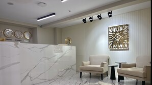 A reception area with a marble reception desk, two beige armchairs, a small round table, and a decorative wall piece. - Daric Hotels (Atakum)