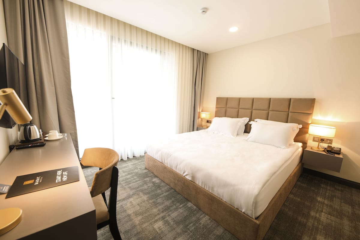 A hotel room with a large bed, a desk with a chair, a lamp, and a nightstand with a phone.