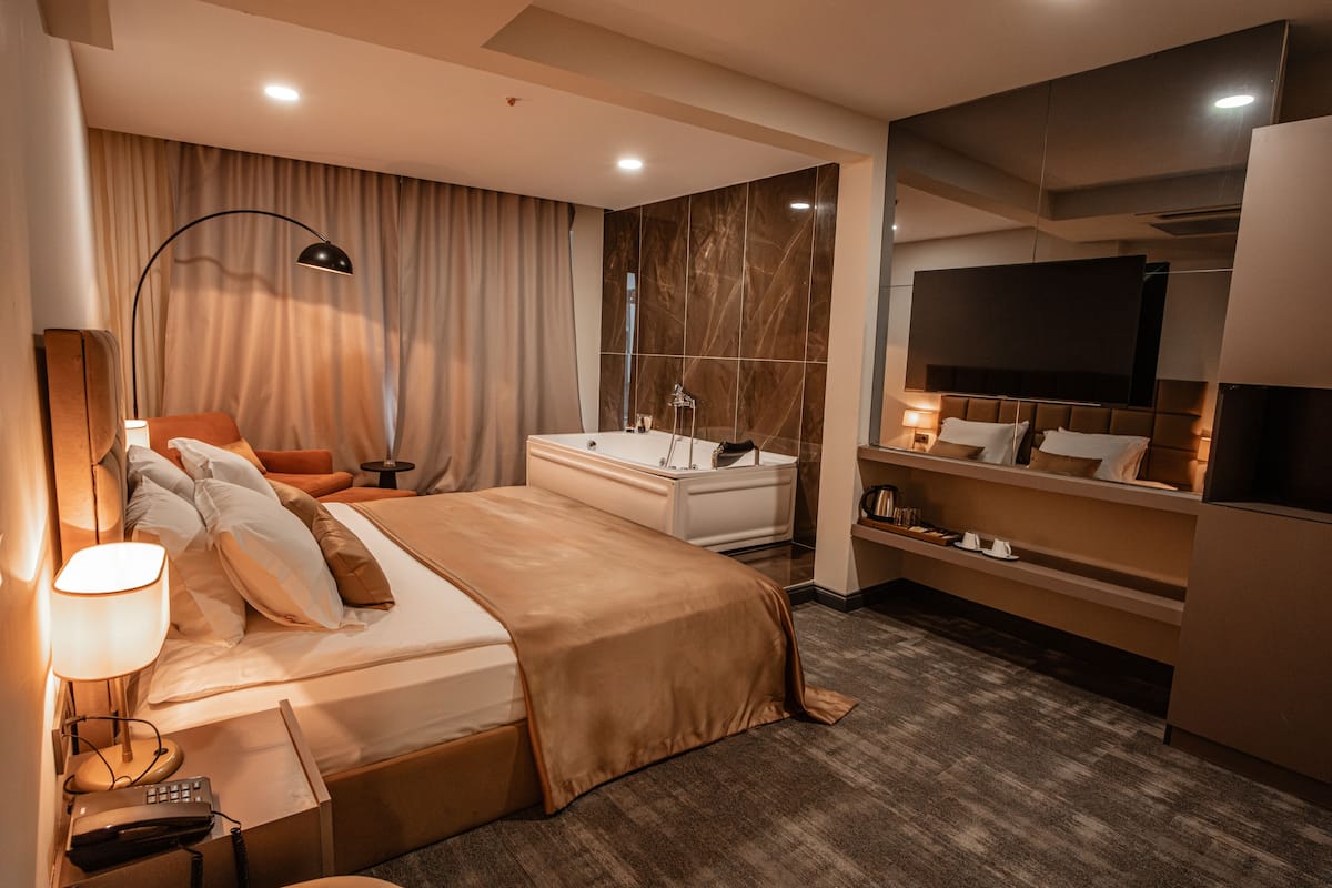 A modern hotel room with a large bed, a desk, a vanity, and a television.