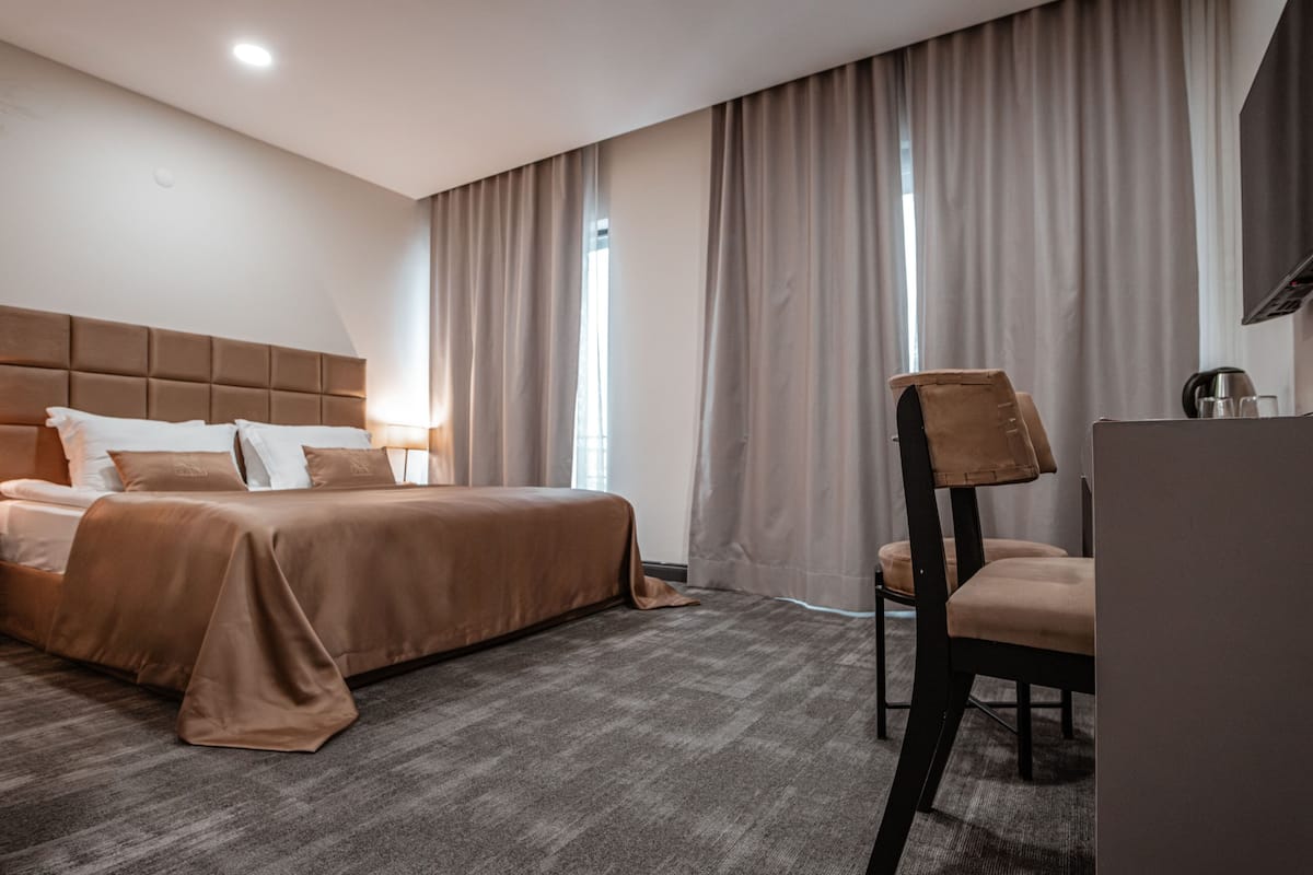 A hotel room with a large bed, a chair, a flat-screen TV, and a window with curtains.