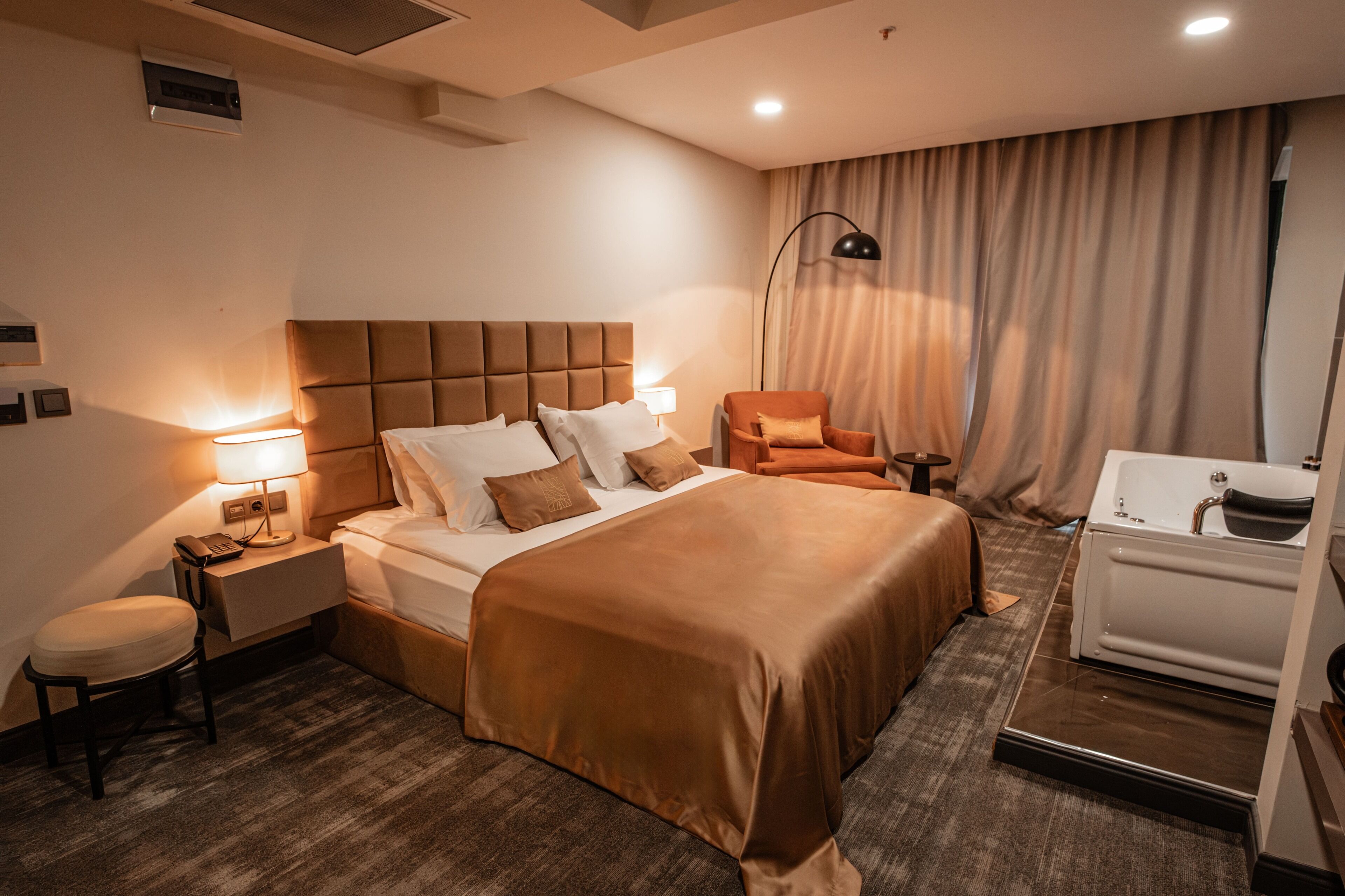 A hotel room with a large bed, a chair, a desk, a lamp, and a bathtub.