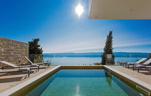 Ein rechteckiger Pool mit klarem Wasser, umgeben von Liegestühlen und einer Steinmauer.
