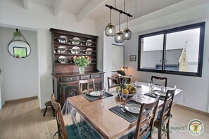 Uma área de refeições com uma mesa de madeira posta para quatro pessoas, um suporte decorativo para pratos e um laptop sobre a mesa.