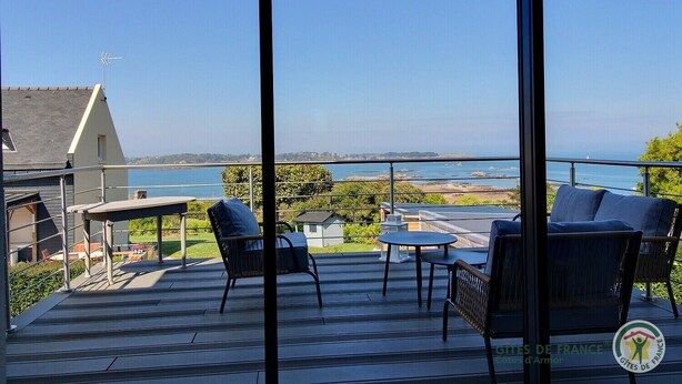 Un balcon avec un espace salon extérieur, une table et une vue sur la mer et la côte.