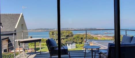 Un balcón con mobiliario exterior, una mesa y vistas al mar y la costa.