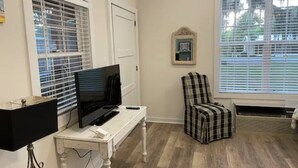 A room with a television on a white table, a plaid chair, and a window with blinds. - Great One Room with Full Bath Guest House! (Darien)