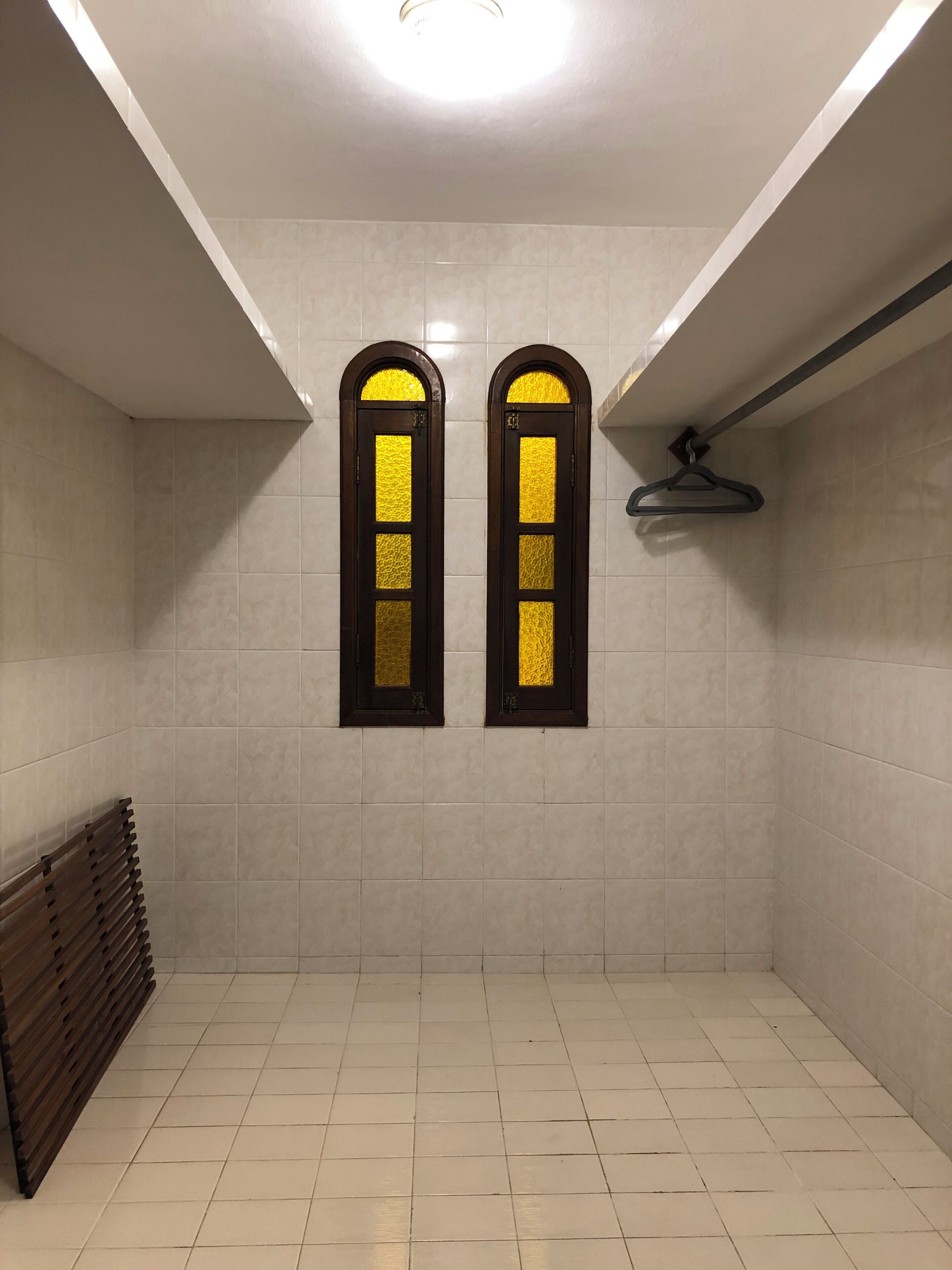 Un baño limpio con baldosas, dos ventanas de arco y un toallero para la ducha colgado.